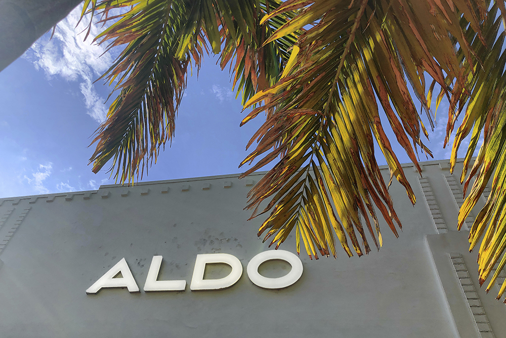 Aldo retail shoe store logo is framed in a palm tree in the Lincoln Road district of Miami Beach, Florida, Thursday, June 6, 2019. The Aldo Group is a Canadian retailer that owns and operates a worldwide chain of shoe and accessories stores, founded by Aldo Bensadoun in Quebec in 1972 .(AP Photo/NewsBase)